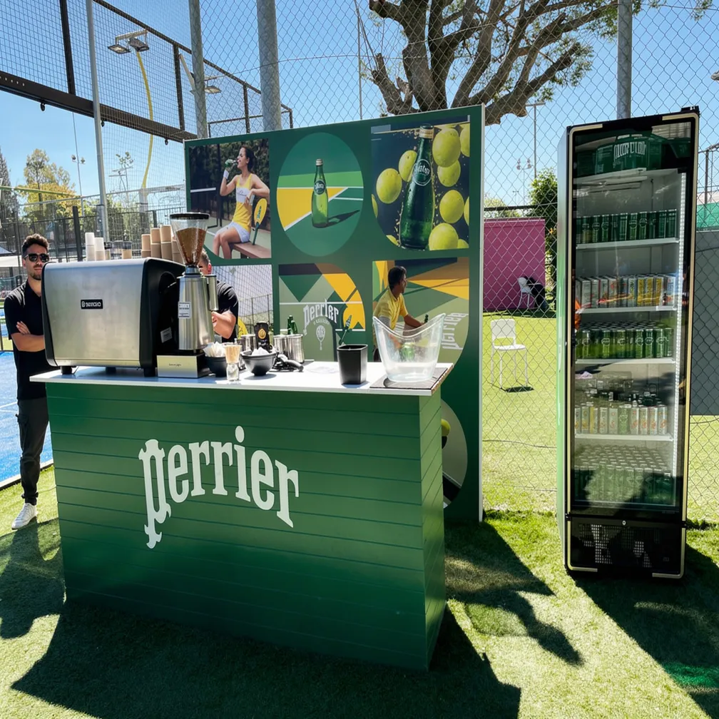 A green Perrier-branded bar counter on the padel court